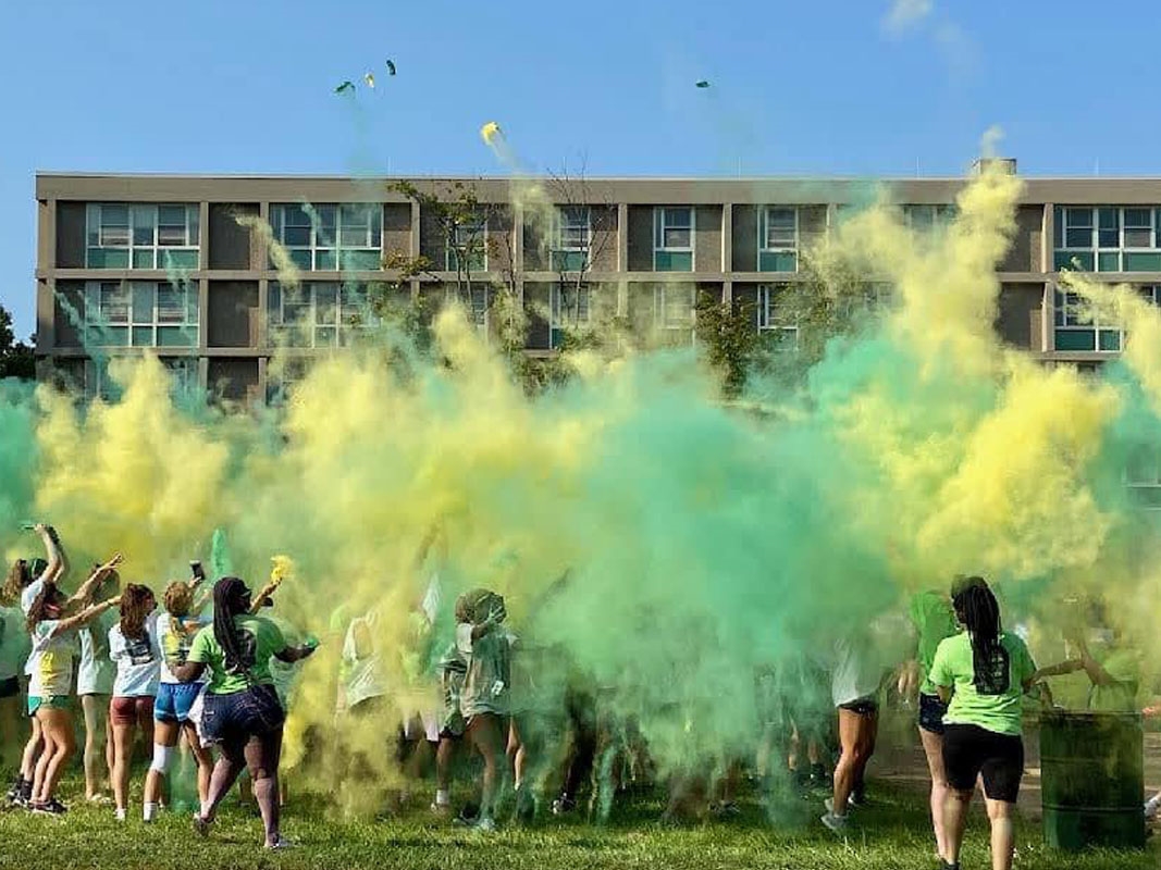 Students in field with green and yellow cloud after color run event.